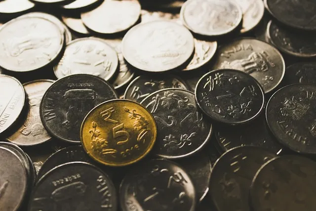 A collection of assorted international coins spread across a surface, photographed by Rupixen on Unsplash